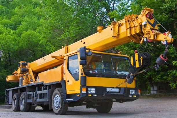 Yellow mobile crane truck parked on a road beside green trees