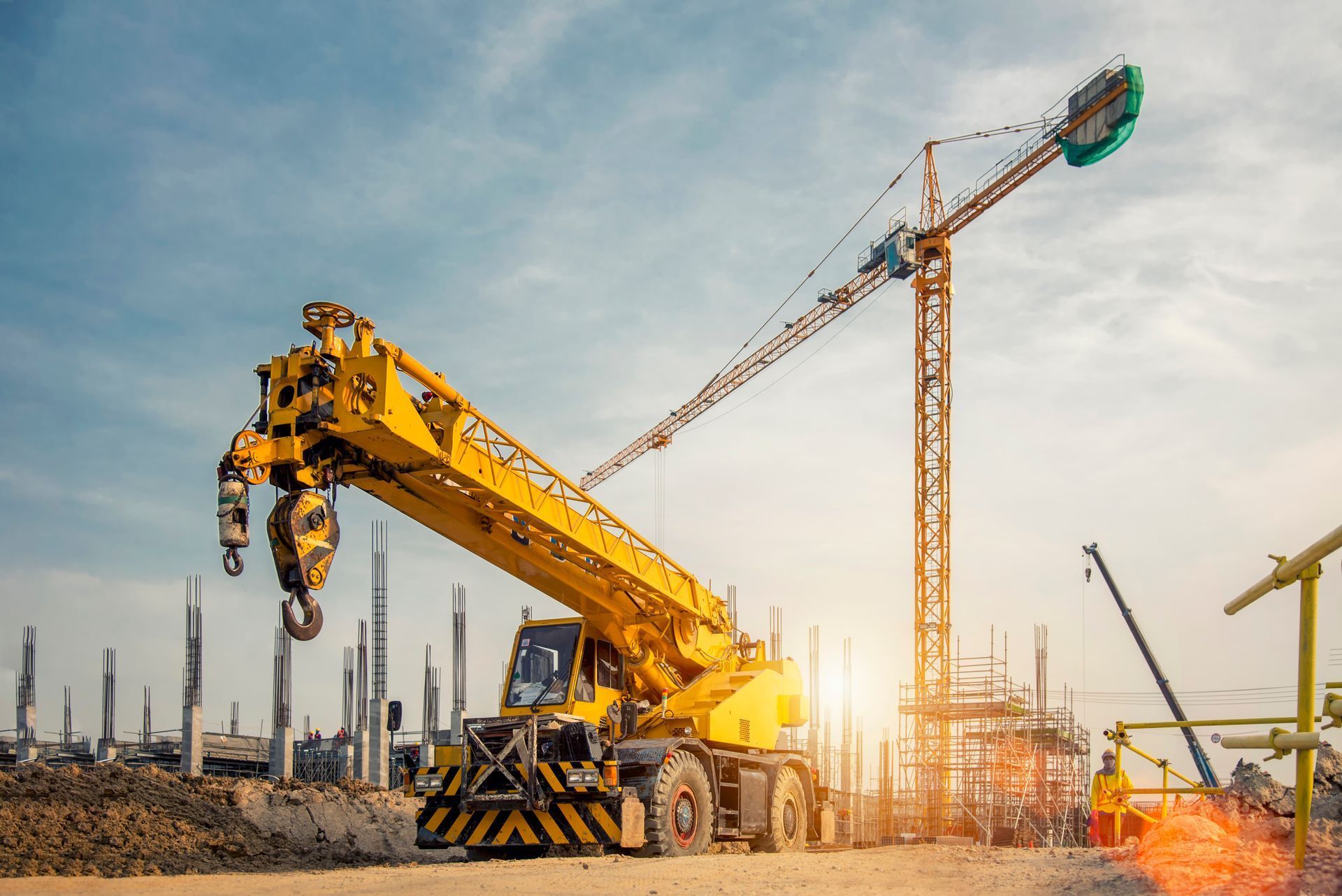 Yellow construction crane at a building site with workers and another crane in the background at sunset