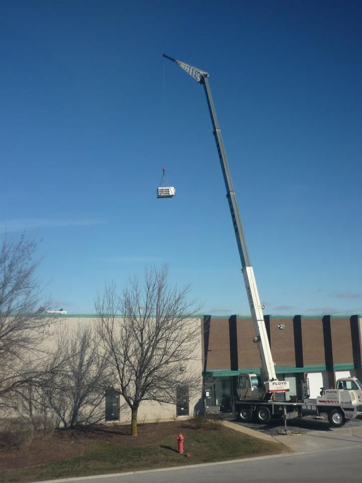 Crane lifting a small load beside a building under a clear blue sky