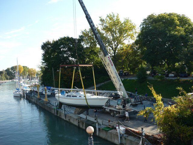 Sailboat on a dock beside a crane, with calm water and trees in the background