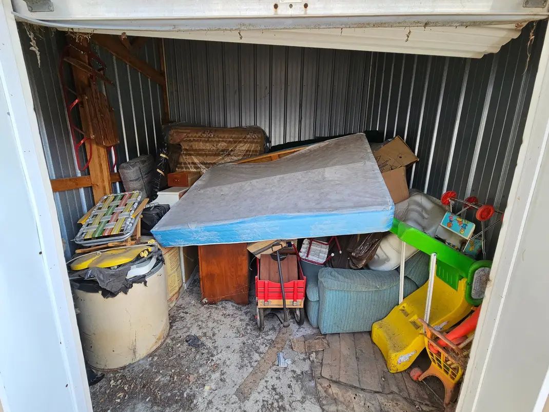 A storage shed filled with lots of junk and a mattress.