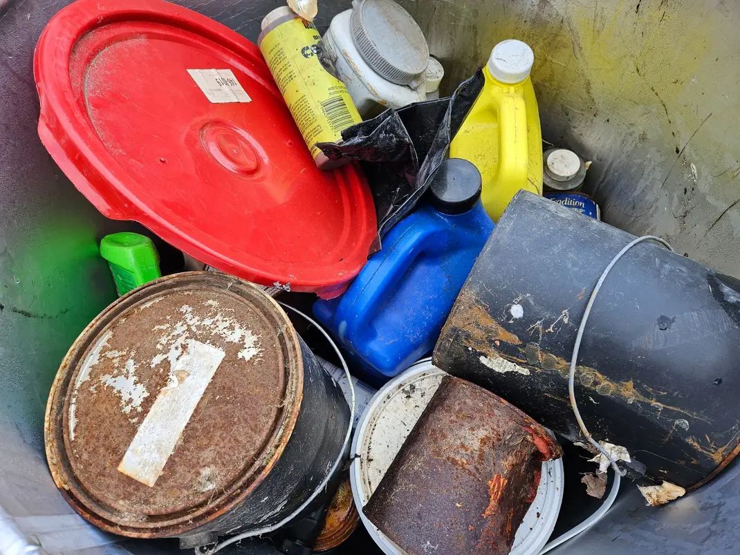 A trash can filled with buckets, bottles, and a red lid.