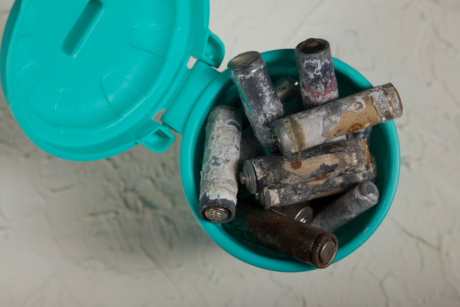 A blue trash can filled with old batteries on a table.