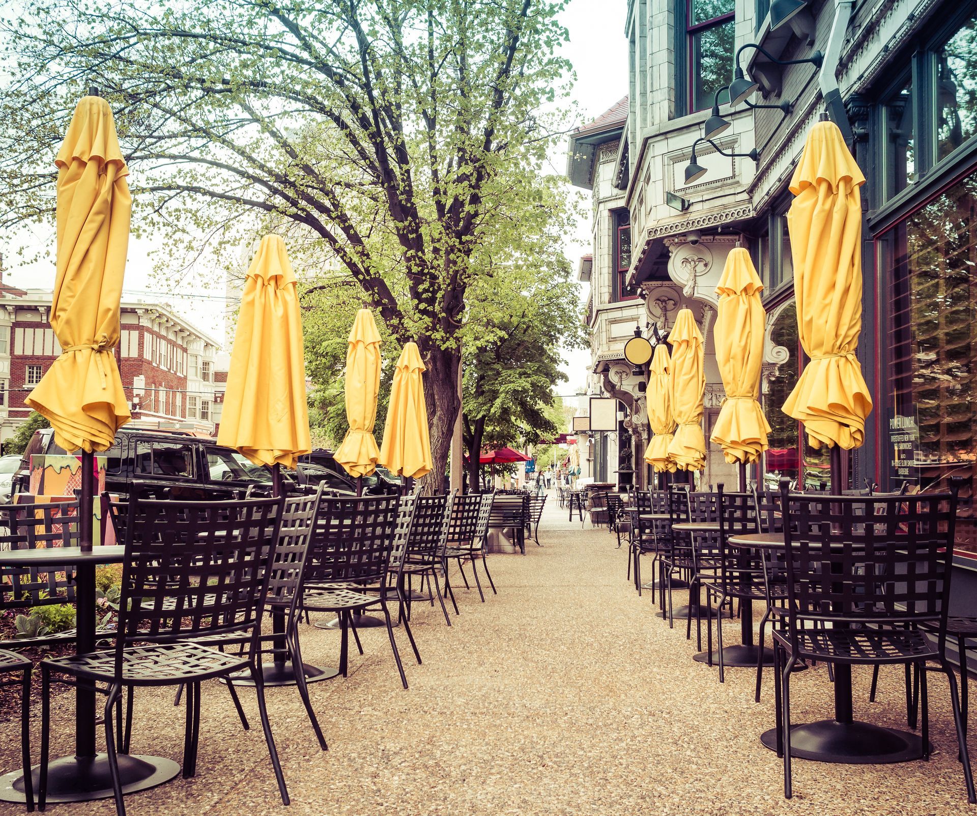 A row of tables and chairs with yellow umbrellas in front of a building