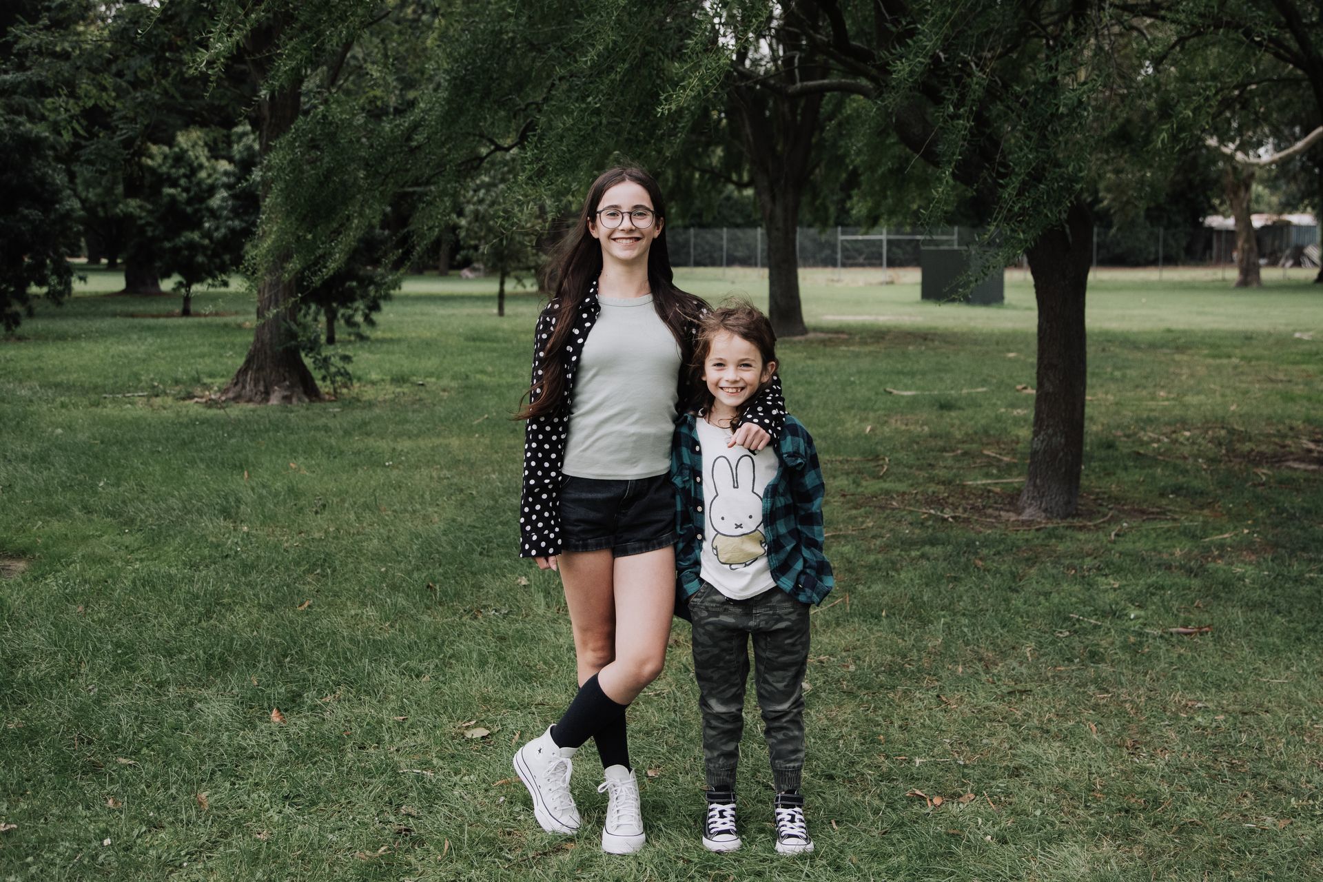A girl and a boy are standing next to each other in a park.
