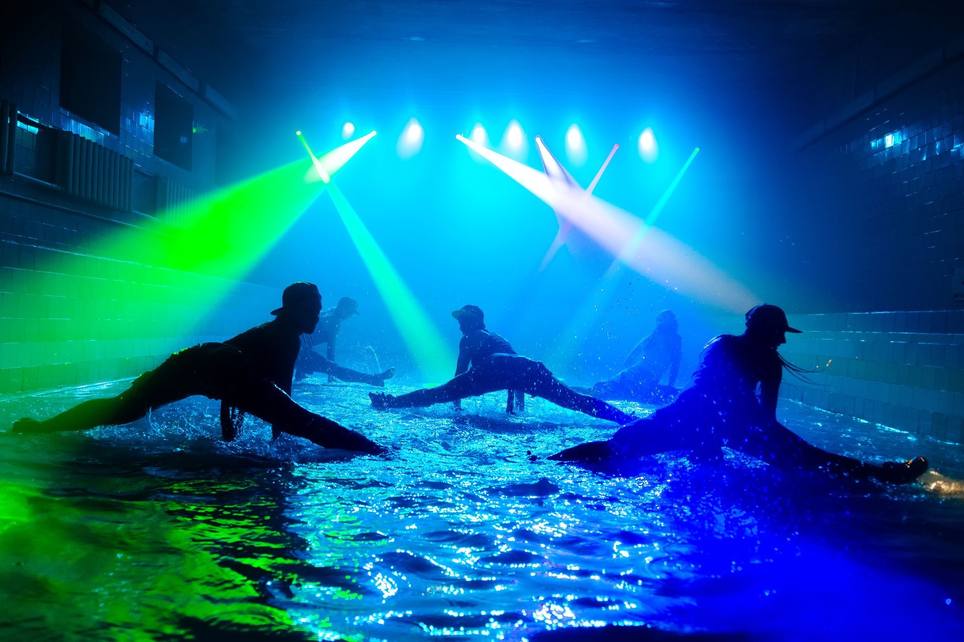 Silhouettes of dancers performing splits in a dramatic light show with water effects, showcasing high-energy choreography similar to a Twerk and Dancehall Workshop, but without water at the actual event