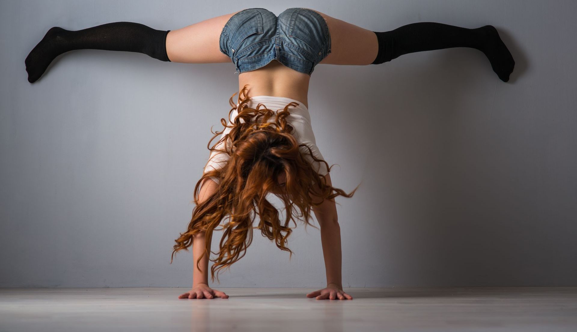 Woman performing a wall twerk handstand in denim shorts and knee-high socks during a Twerk and Dancehall Workshop