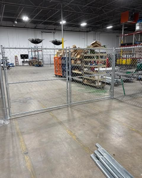 Chain-link fence inside a warehouse, with a gated entryway and materials stacked in the background.