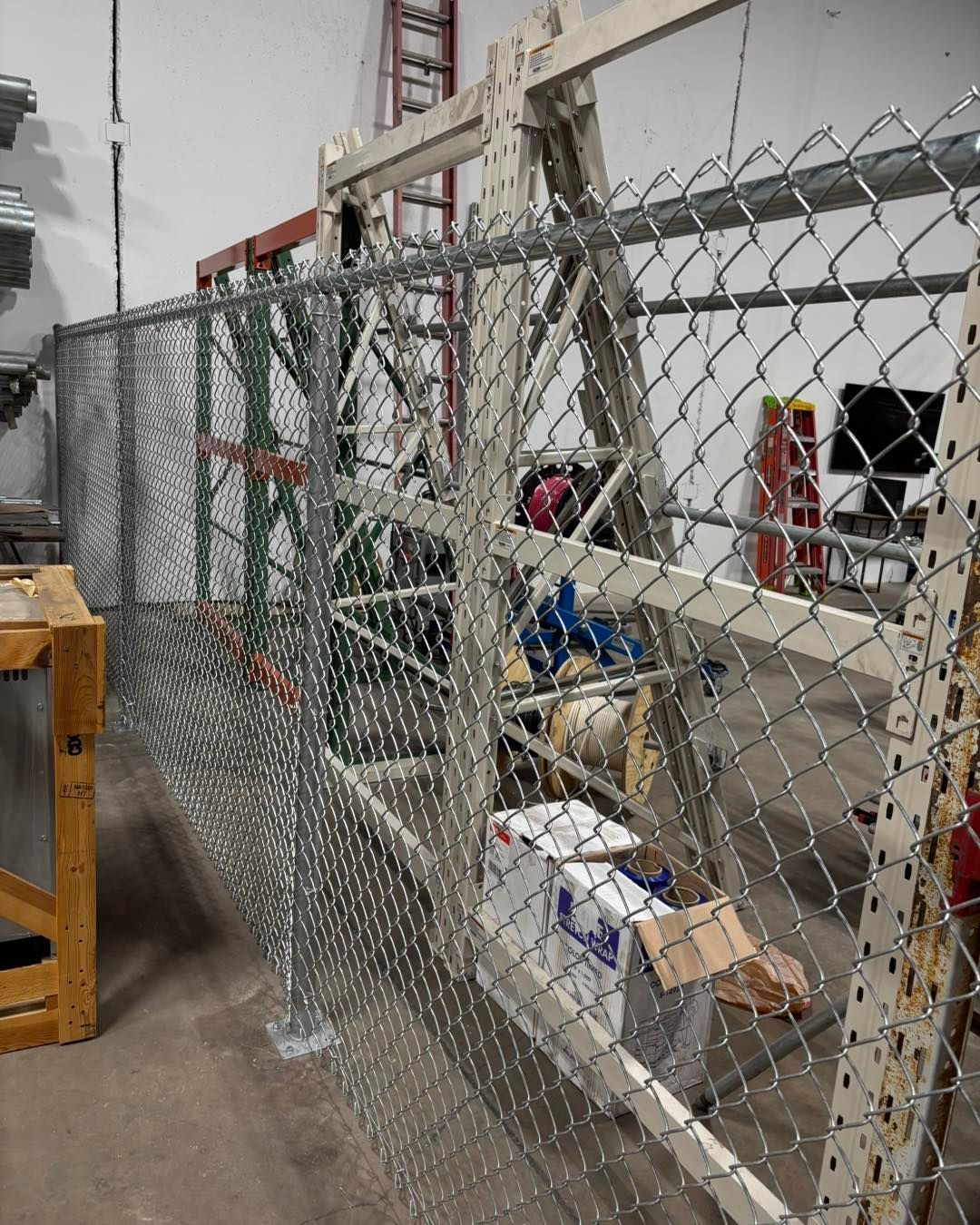 Chain-link fence partially constructed within a warehouse, attached to a metal frame.