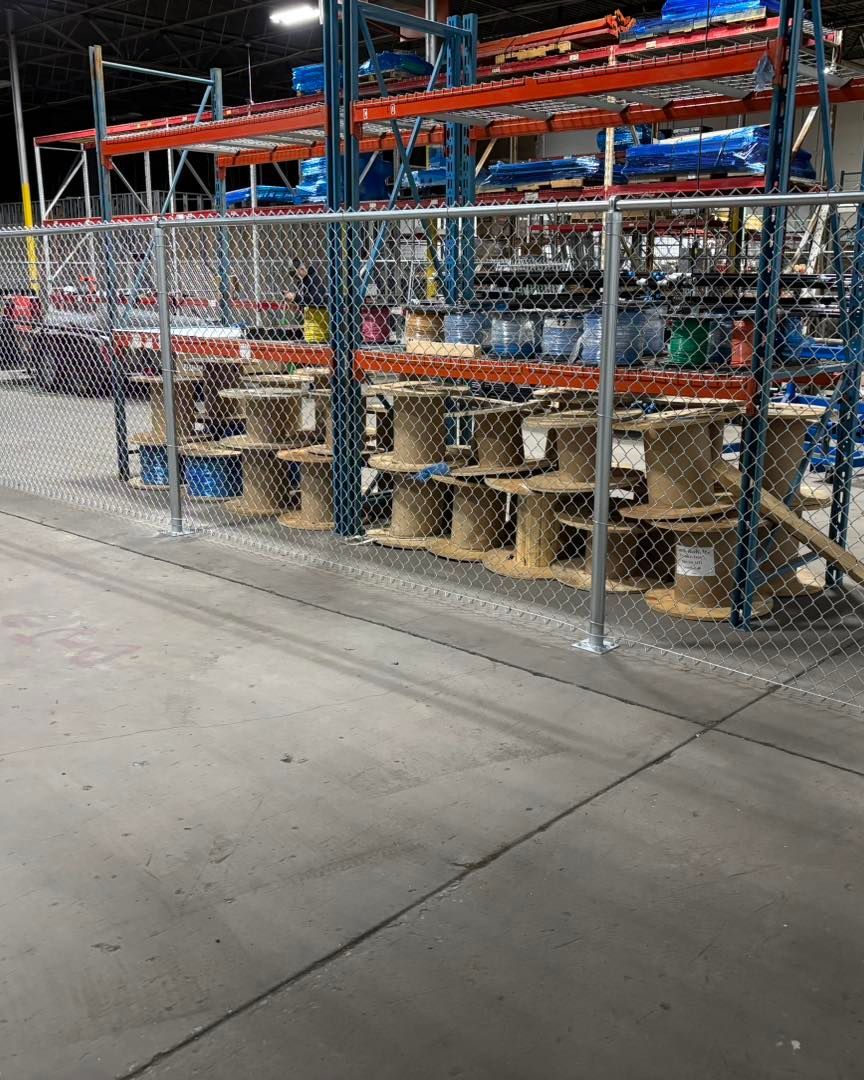 Warehouse interior with spools of wire behind a chain-link fence; shelving units with materials in the background.