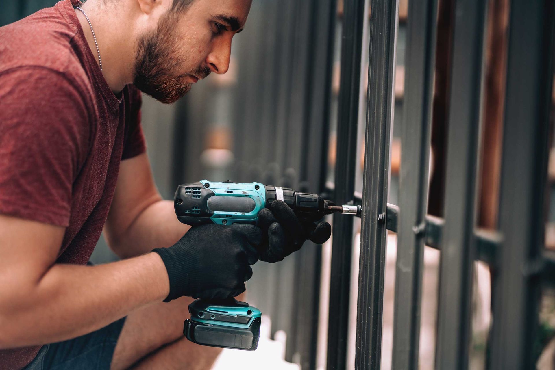 Focused installer fastening vertical metal fence bars securely with power drill.