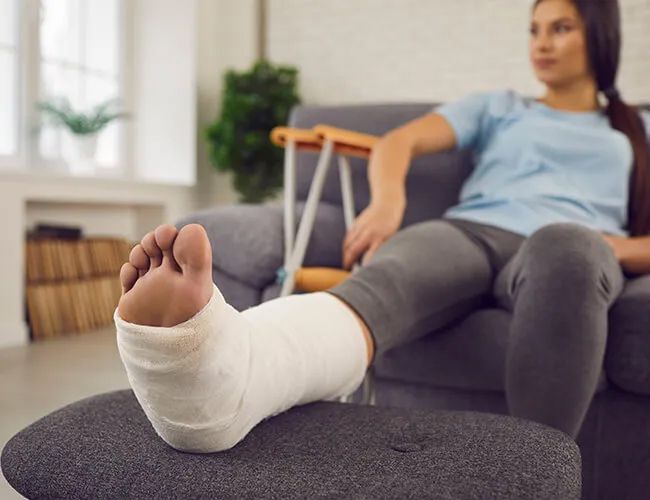 a woman with a cast on her leg is sitting on a couch .