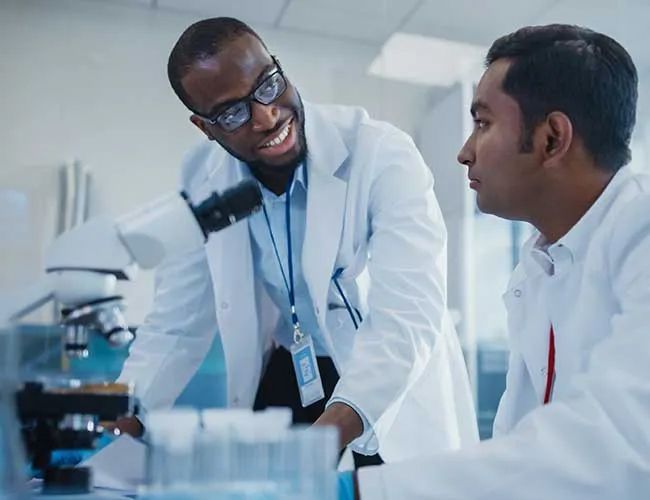 two men in lab coats are looking through a microscope in a laboratory .