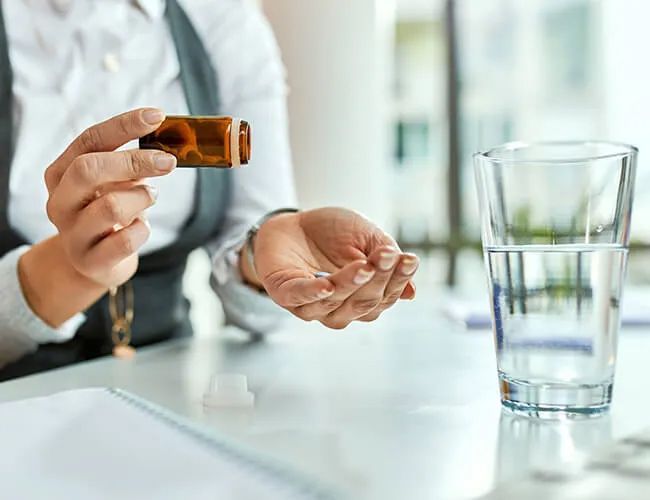 a woman is pouring a pill into her hand next to a glass of water .
