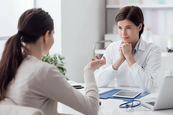 a woman is sitting at a table talking to a doctor .