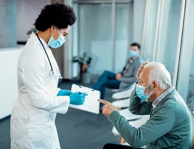 a doctor is talking to an older man wearing a mask in a hospital waiting room .
