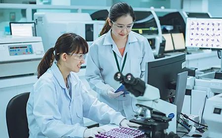 two female scientists are working in a laboratory looking through a microscope .
