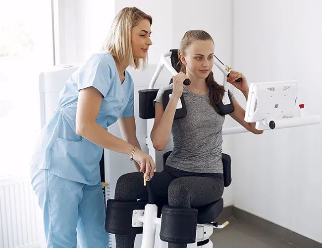a woman is sitting on a machine with a nurse standing next to her .