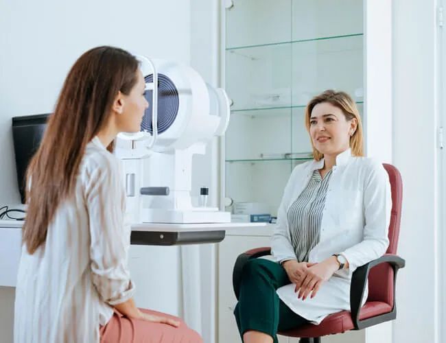 a woman is sitting in a chair talking to an ophthalmologist .