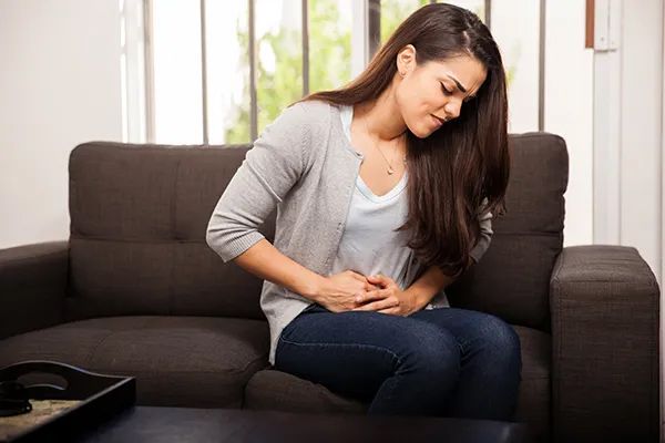 a woman is sitting on a couch holding her stomach in pain .