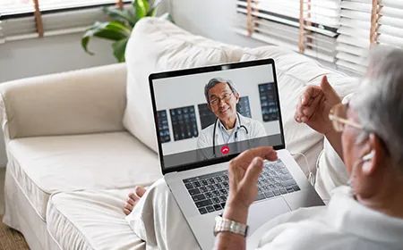 an elderly man is sitting on a couch talking to a doctor on a laptop computer .