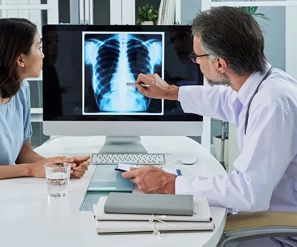 a doctor is pointing at an x-ray of a woman 's chest on a computer screen .