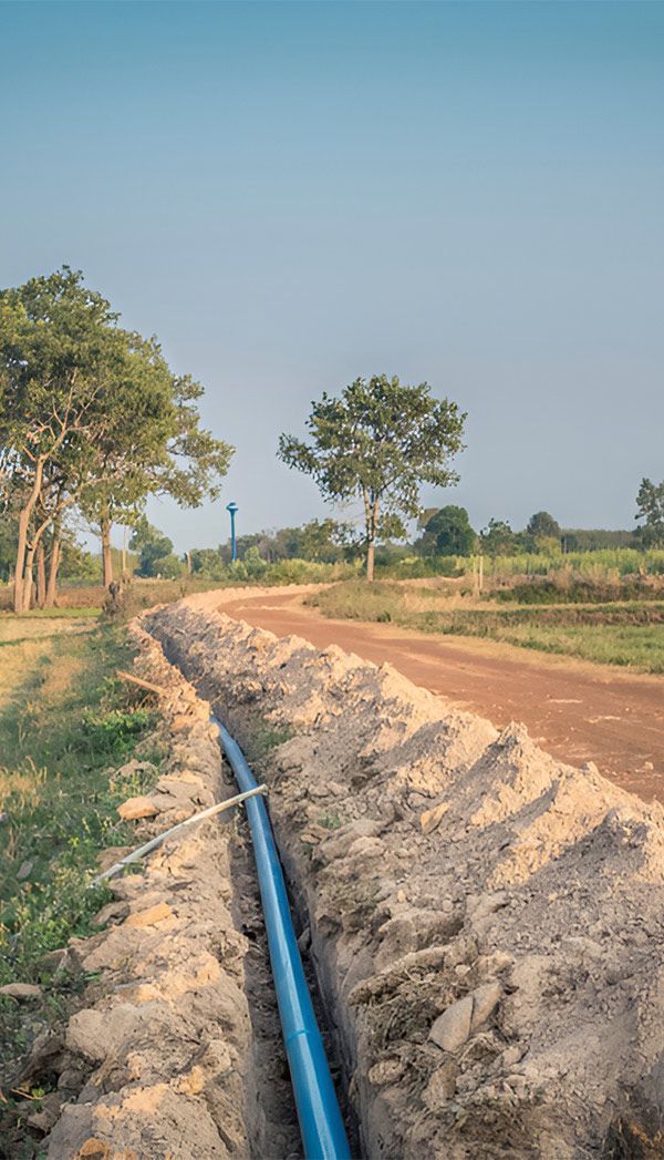 A Blue Pipe is Being Installed in the Dirt Next to a Dirt Road — Elite Wastewater Solutions in Bowral, NSW