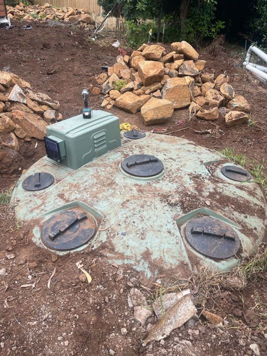 A Septic Tank is Sitting in the Dirt Next to a Pile of Rocks — Elite Wastewater Solutions in Moss Vale, NSW