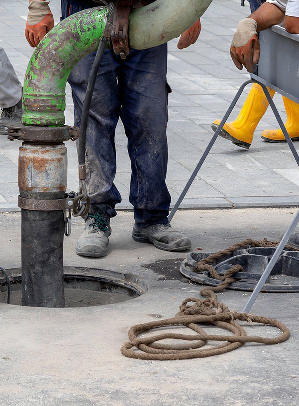 A Man is Pumping a Green Pipe Into a Manhole — Elite Wastewater Solutions in Mittagong, NSW