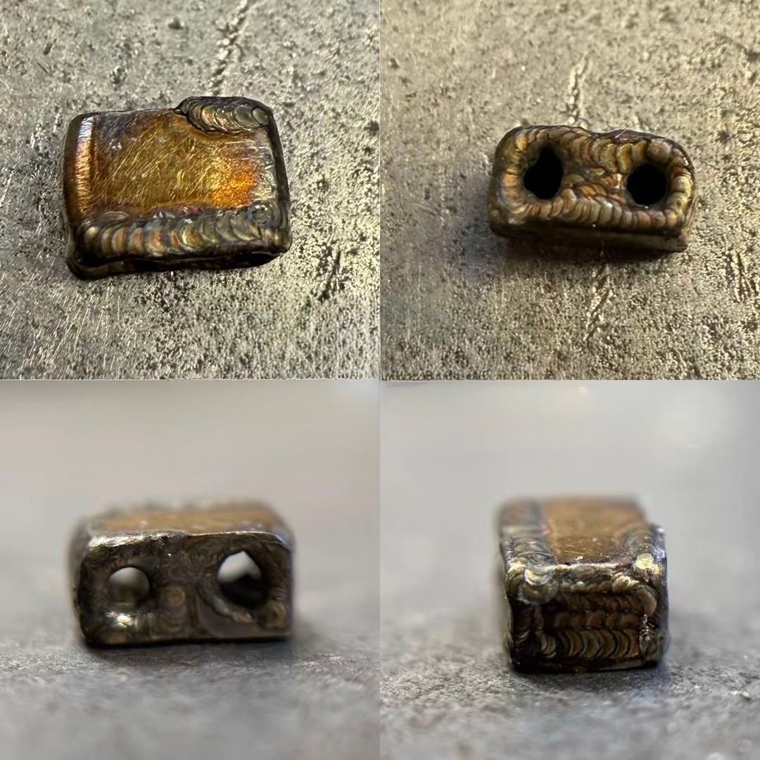 Quattro viste di una piccola perlina metallica rettangolare con due fori, che mostrano le saldature e il centro color oro.