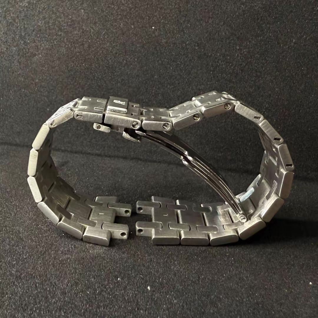 Bracciale per orologio in metallo argentato con chiusura deployante a vista, su uno sfondo scuro e texturizzato.