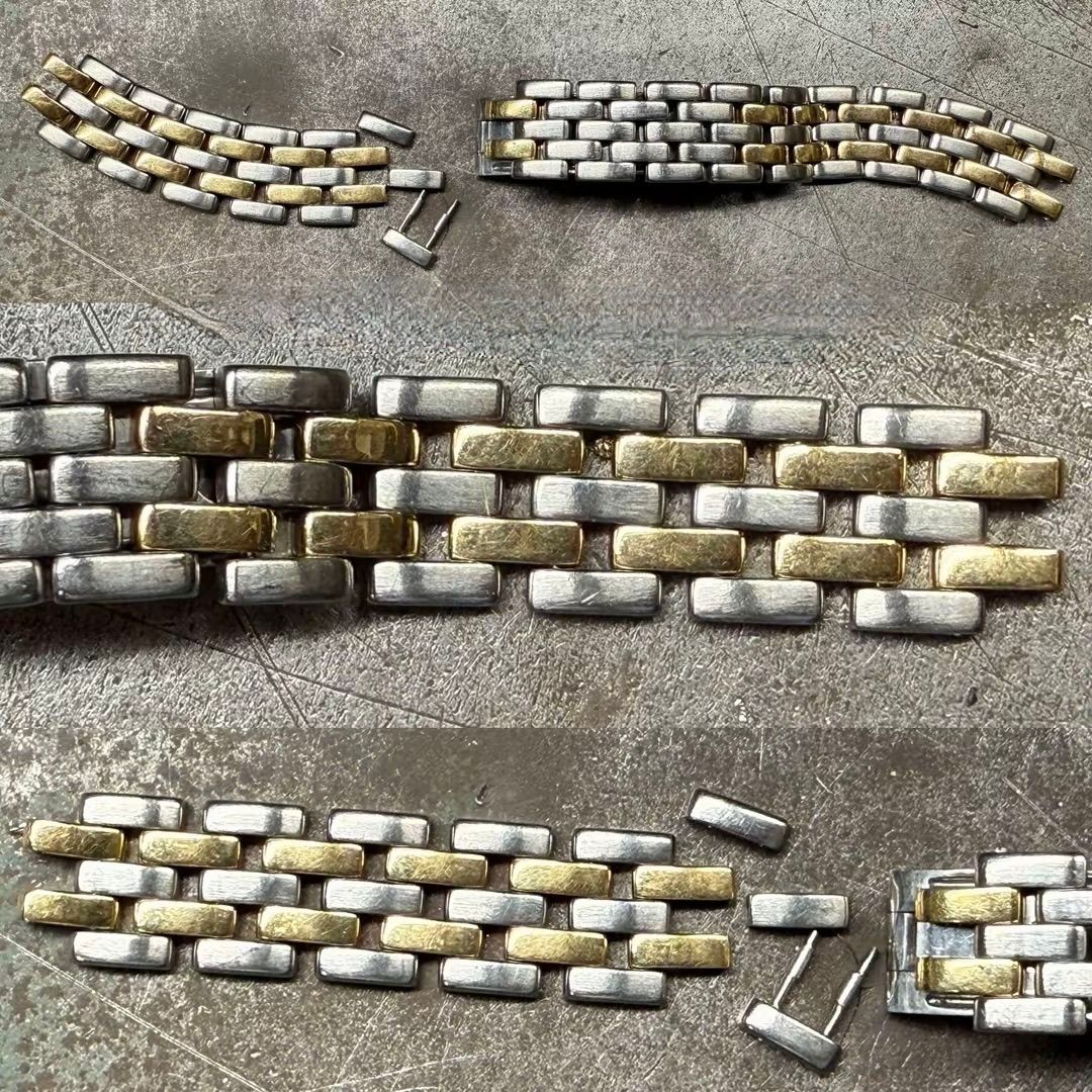 Primo piano di maglie rotte di un bracciale di orologio bicolore argento e oro, disposte su una superficie grigia ruvida.