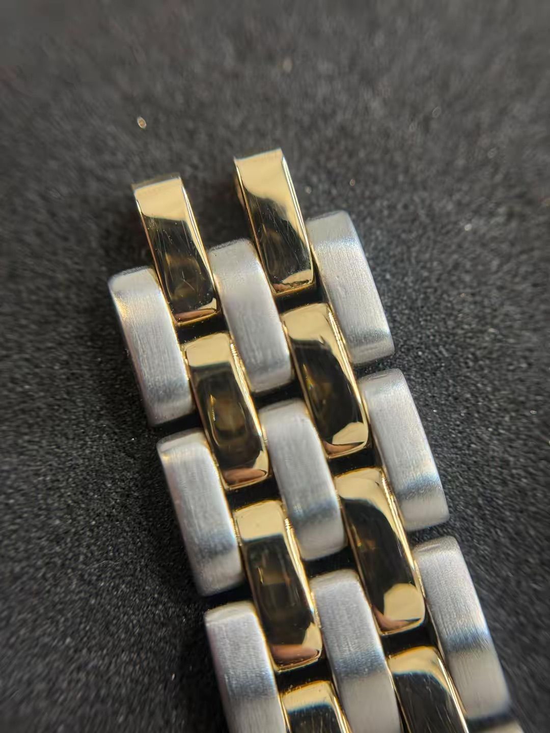 Primo piano di un bracciale per orologio bicolore caratterizzato da maglie rettangolari alternate in argento spazzolato e oro lucido.