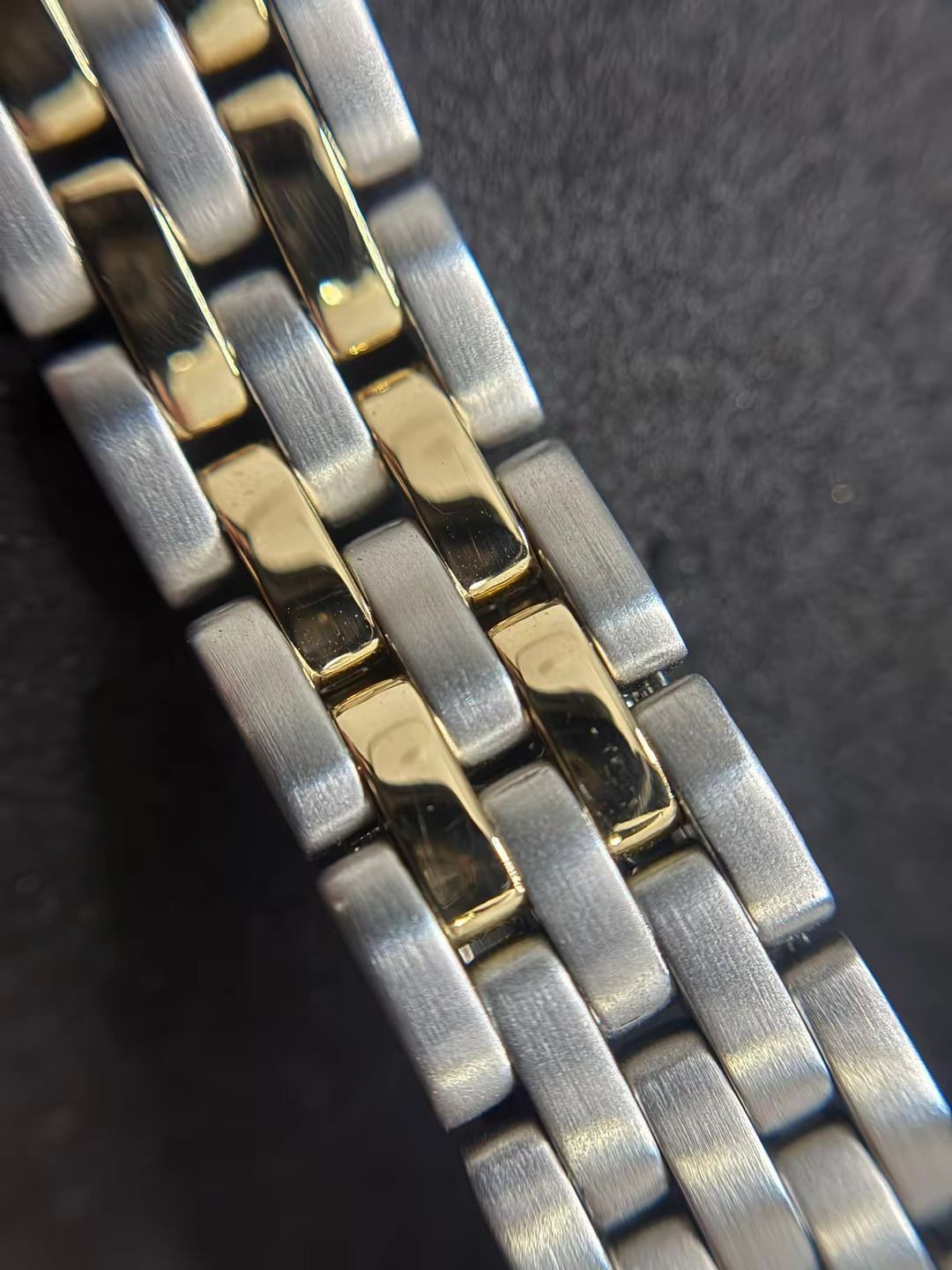 Primo piano di un bracciale per orologio bicolore con maglie in metallo alternate color argento spazzolato e color oro lucido.