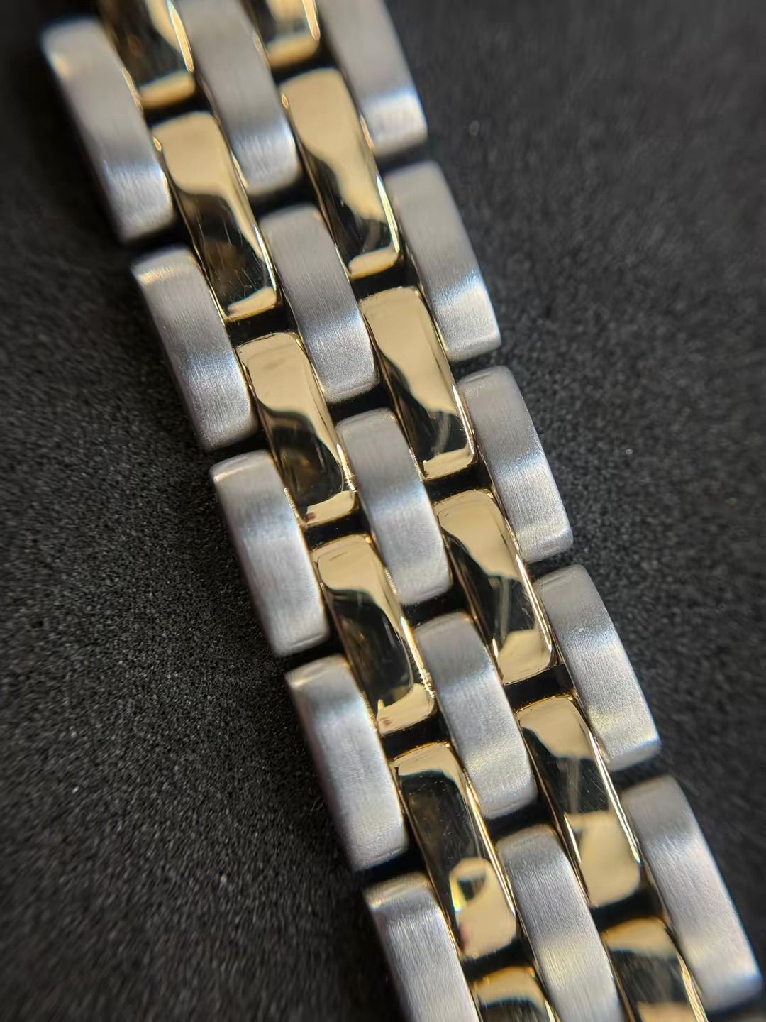 Primo piano di un bracciale per orologio bicolore con maglie in argento spazzolato e maglie centrali color oro lucido.