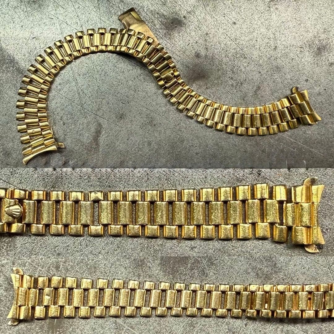 Tre bracciali per orologio in metallo color oro, composti da cinque maglie ciascuno, sono disposti su una superficie grigia e ruvida.