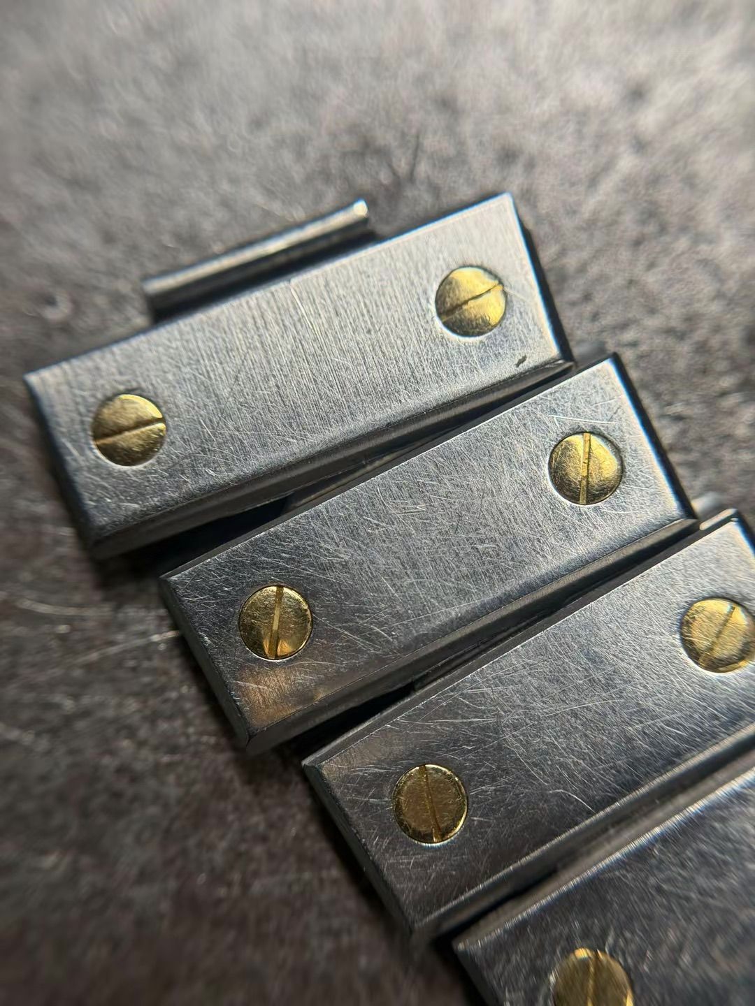 Primo piano di un cinturino di orologio in metallo con maglie rettangolari color argento fissate da piccole viti a taglio color oro.