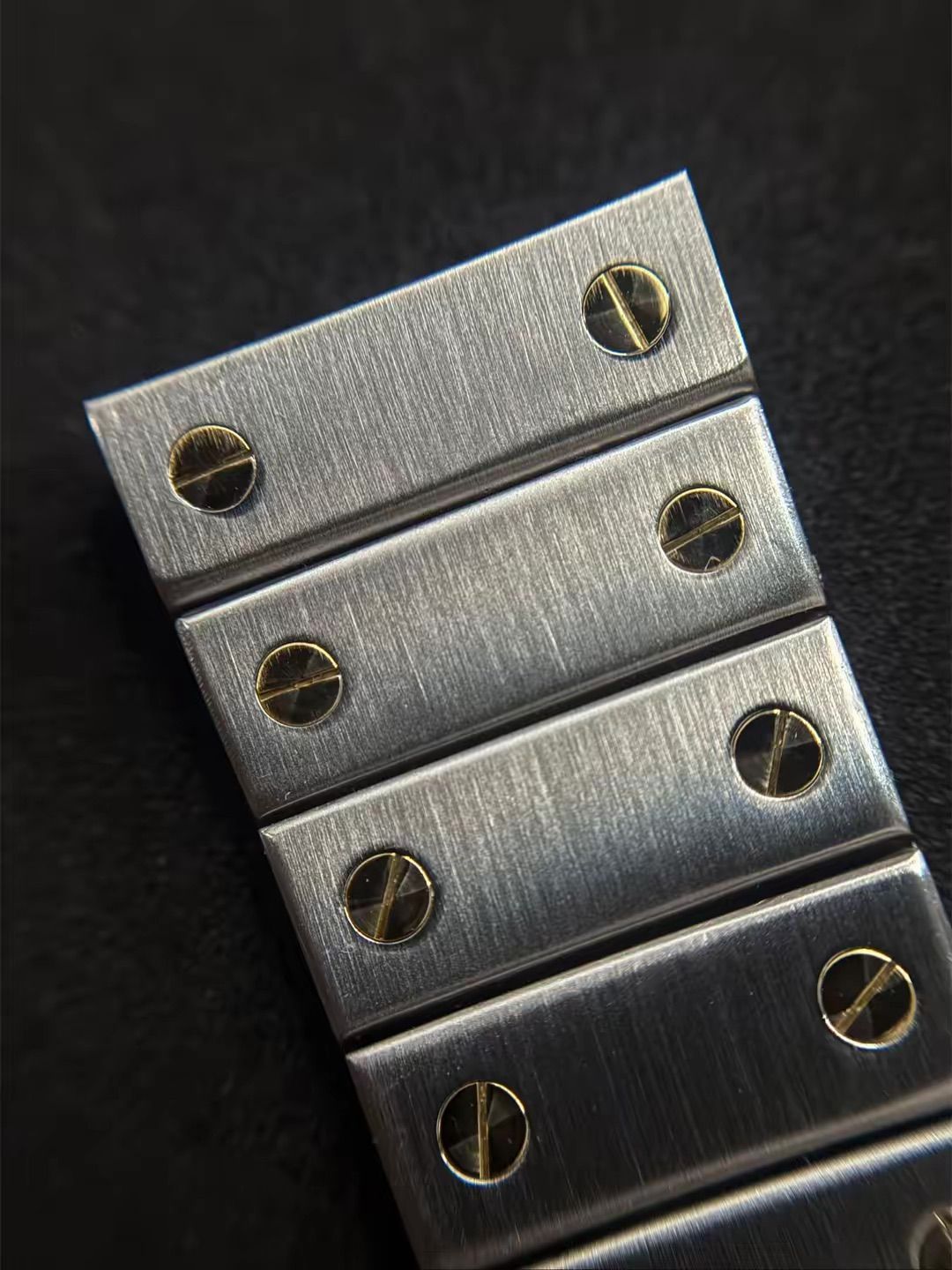 Primo piano di un cinturino per orologio in metallo spazzolato con viti a taglio color oro su entrambi i lati delle maglie.