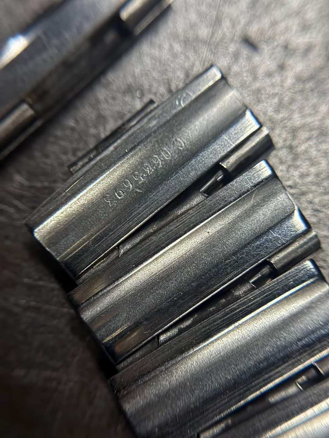 Una vista ravvicinata e angolata di un bracciale metallico per orologio, con particolare attenzione al codice identificativo impresso sulle maglie.