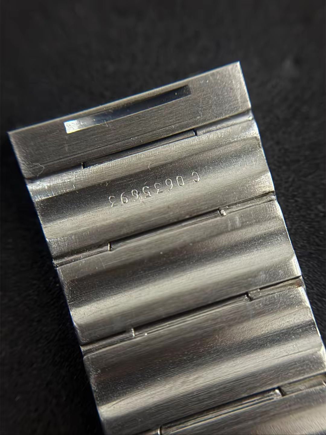 Primo piano di un bracciale per orologio in argento con una chiusura in metallo su cui è inciso un codice seriale numerico poco visibile.