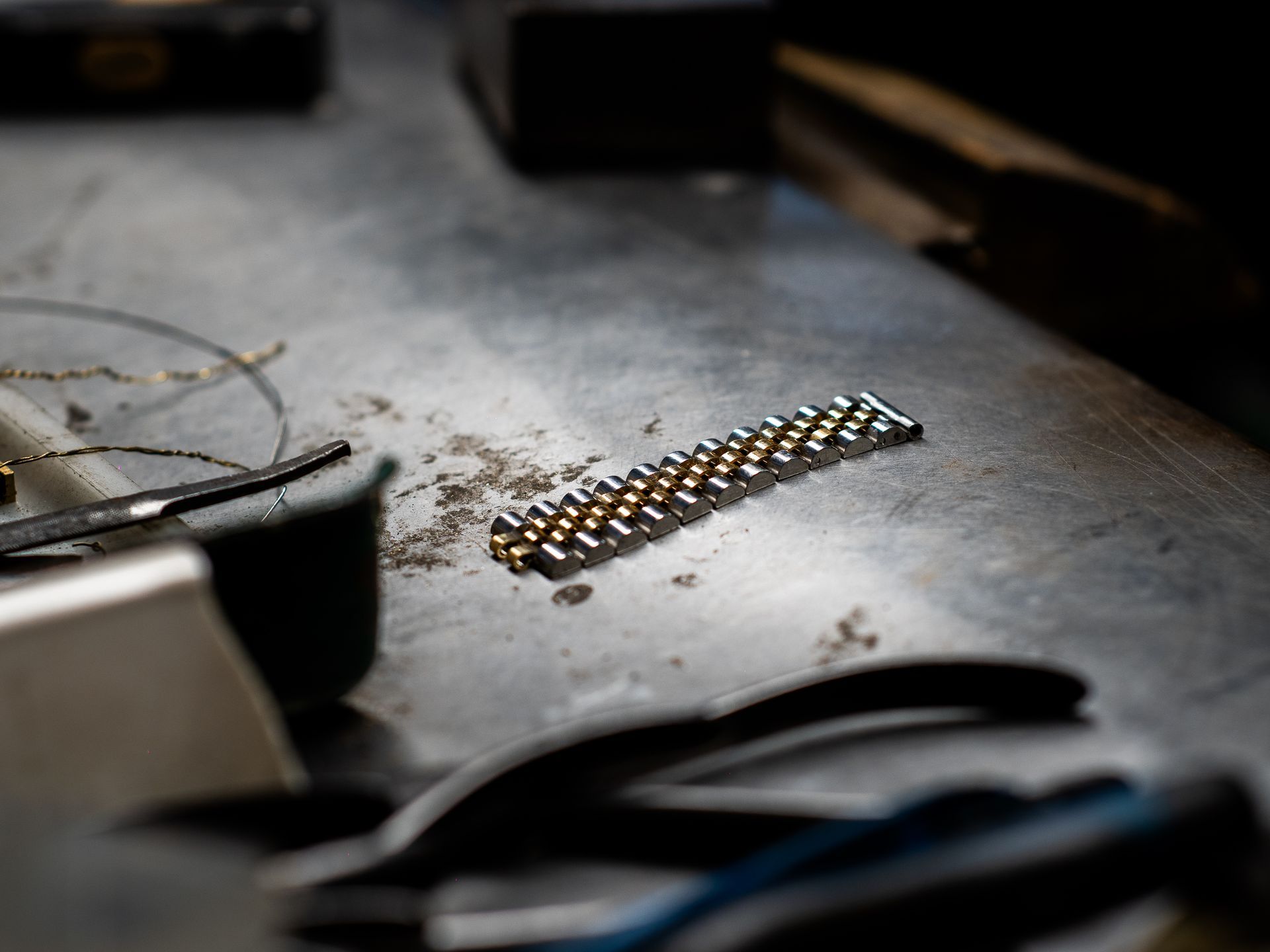 Un bracciale per orologio bicolore, oro e argento, giace su un banco da lavoro circondato da attrezzi.