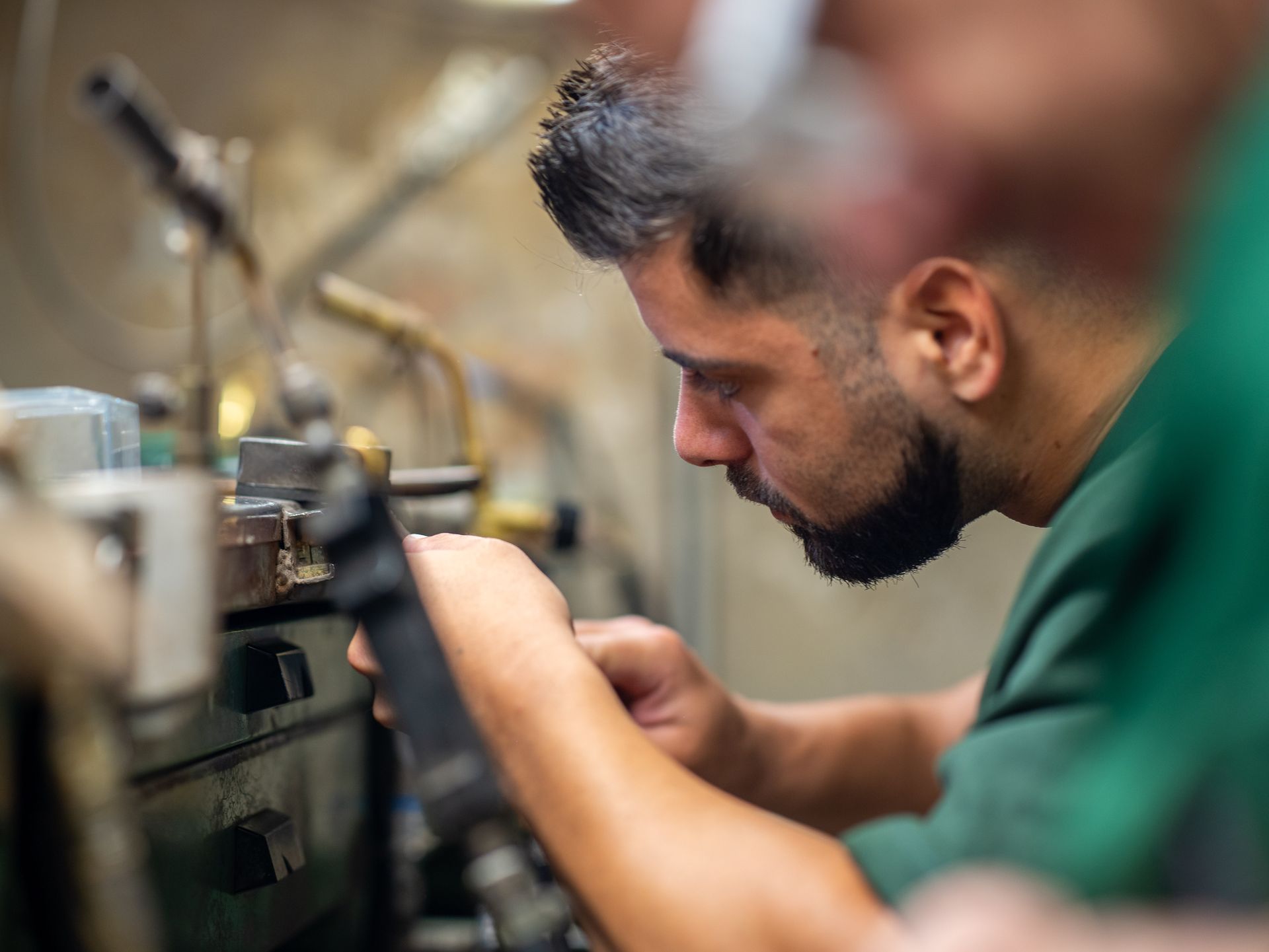 Un gioielliere concentrato lavora a un banco da lavoro con strumenti specializzati, maneggiando con cura un piccolo oggetto di metallo.