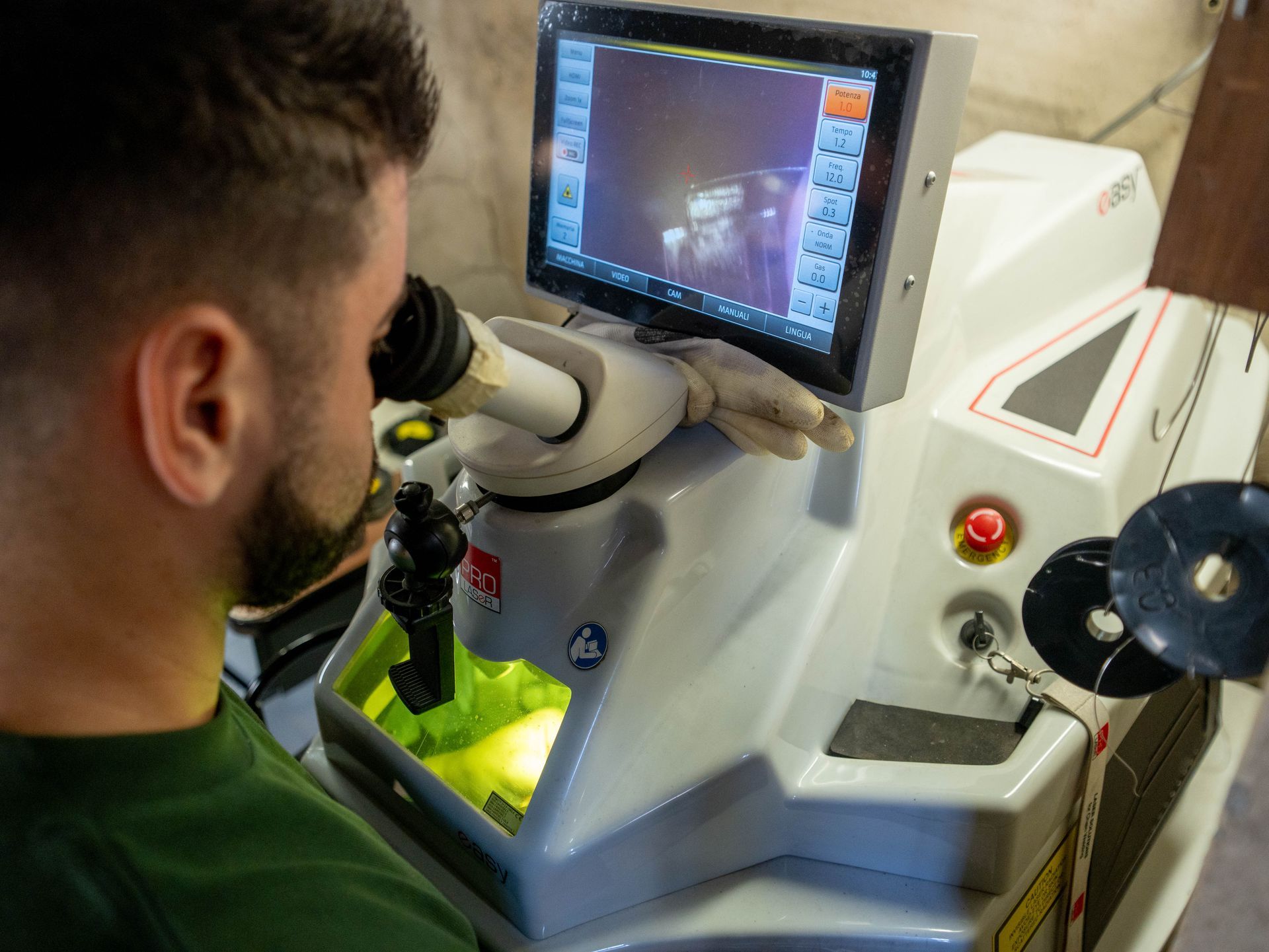 Una persona utilizza un microscopio digitale per ispezionare un piccolo componente, visualizzando l'immagine ingrandita su uno schermo integrato.