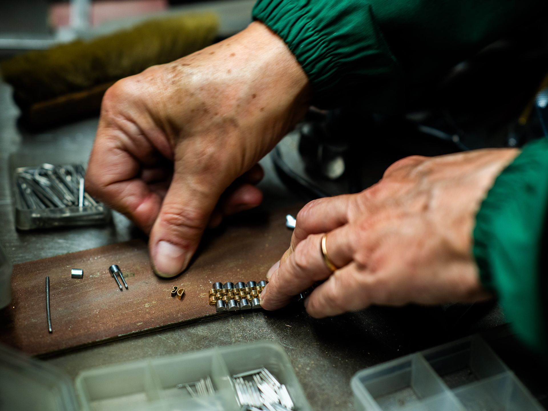 Le mani di una persona assemblano un cinturino metallico per orologio su una superficie di lavoro in pelle, circondata da piccoli componenti e organizer.