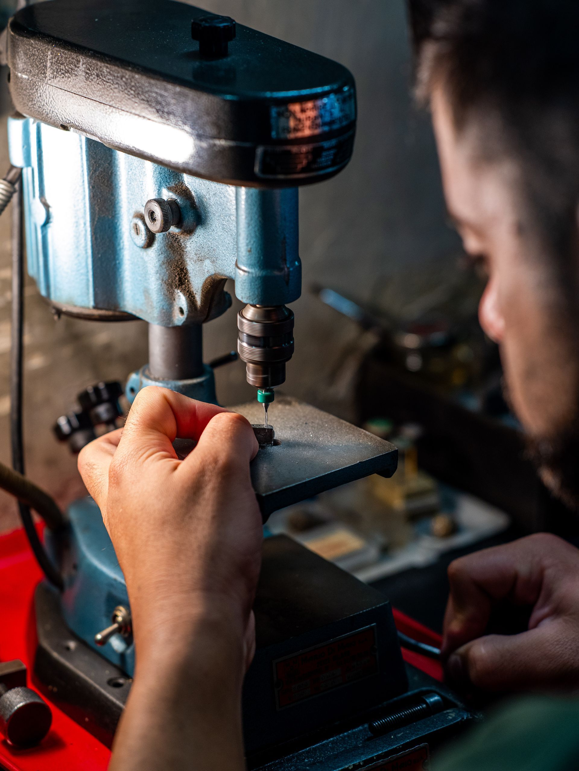 Una persona utilizza un piccolo trapano a colonna blu per lavorare su un minuscolo oggetto su un banco da lavoro.