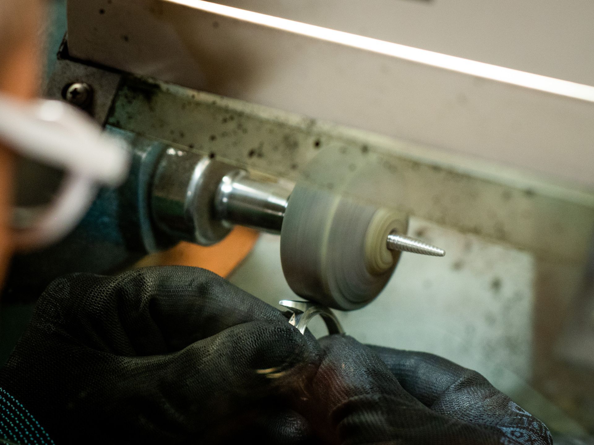 Una persona con indosso guanti neri tiene un anello di metallo contro una mola lucidante industriale in rotazione.