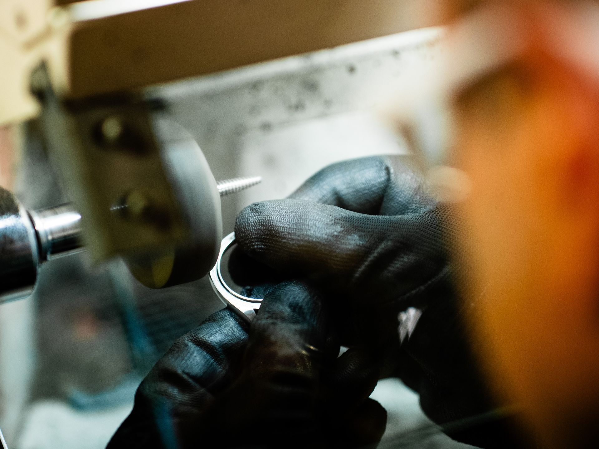 Una persona che indossa guanti protettivi neri utilizza una lucidatrice per lucidare la cassa metallica di un orologio.