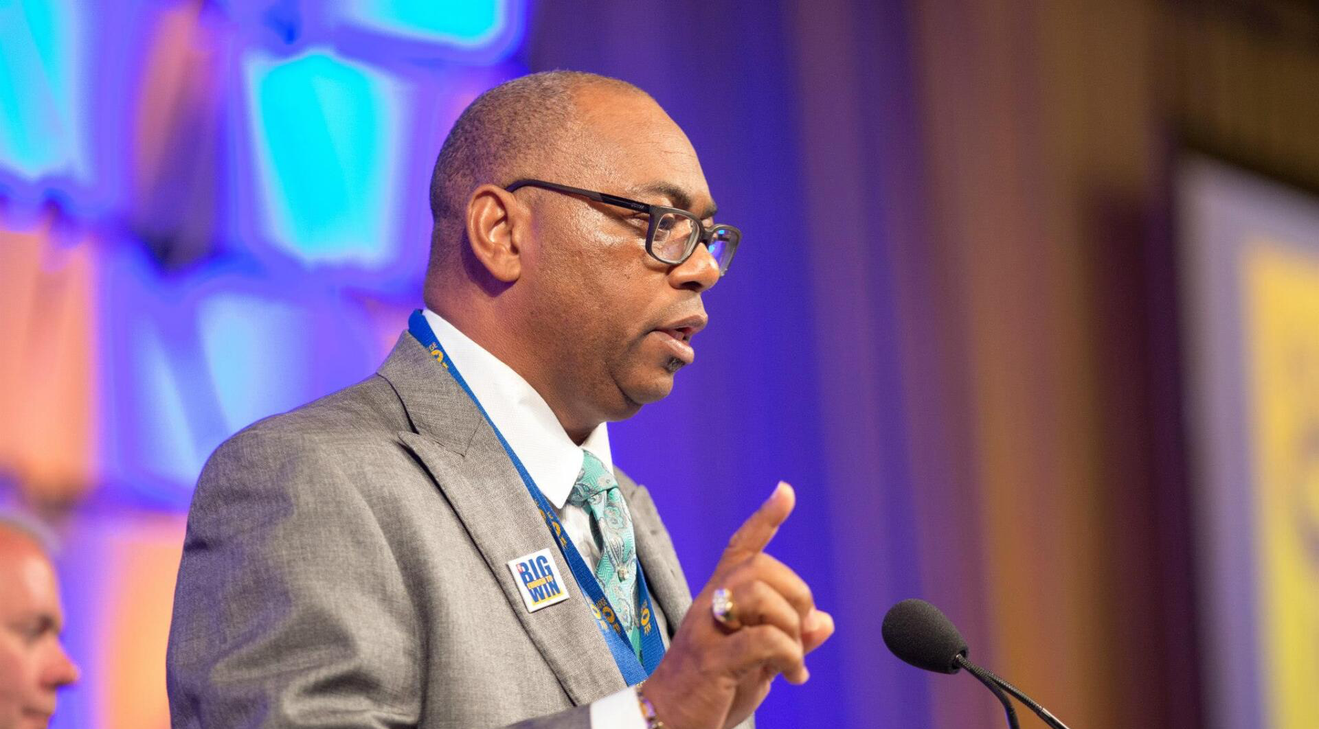 Everett Kelley is giving a speech in front of a microphone at the National Convention.