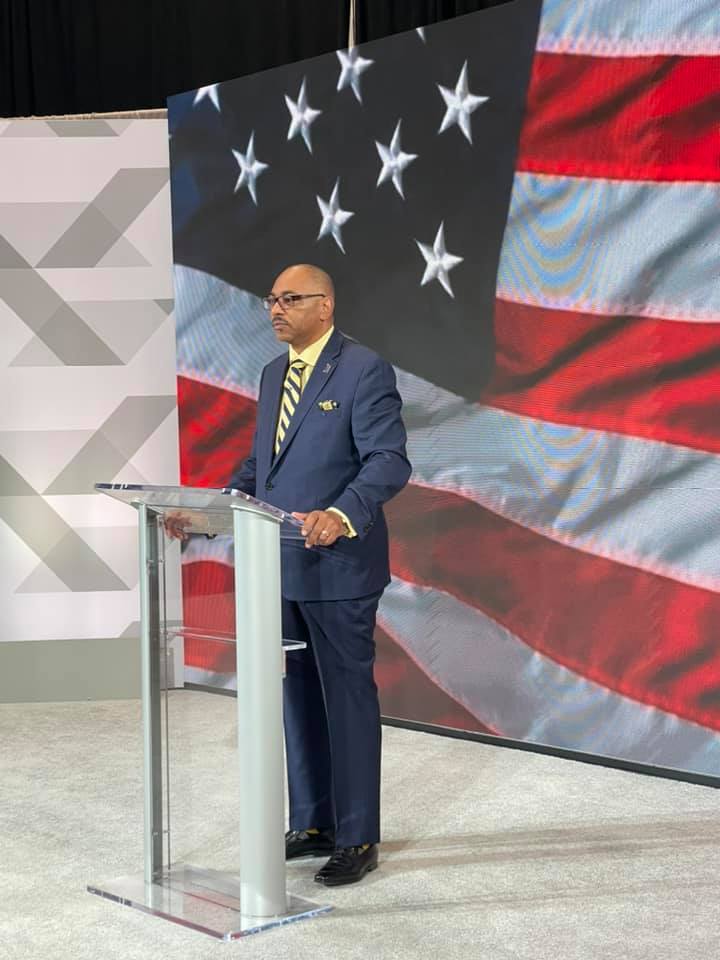 Everett Kelley is giving a speech in front of a microphone at the National Convention.