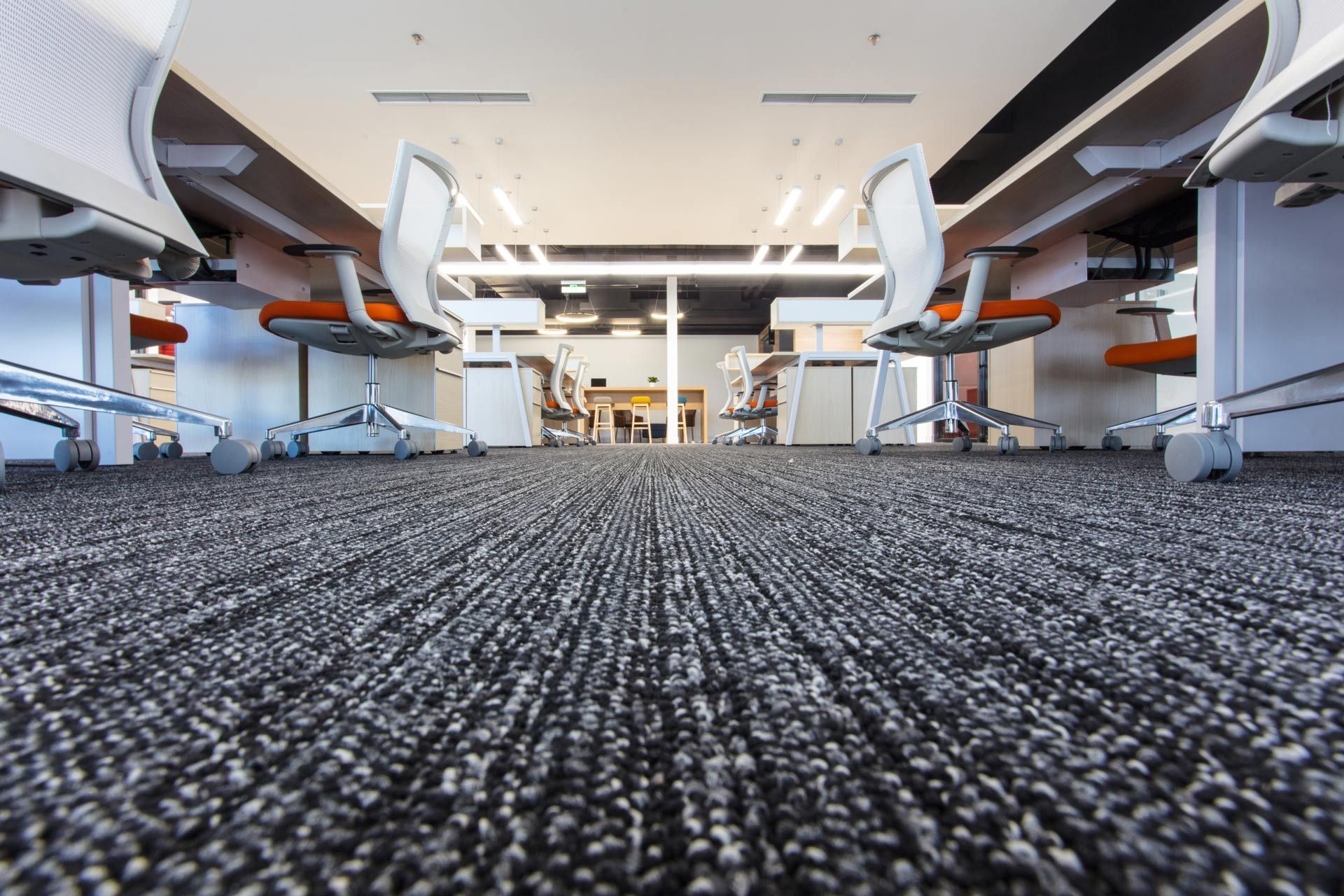 Empty modern office with rows of desks and chairs on a dark carpeted floor, viewed from ground level